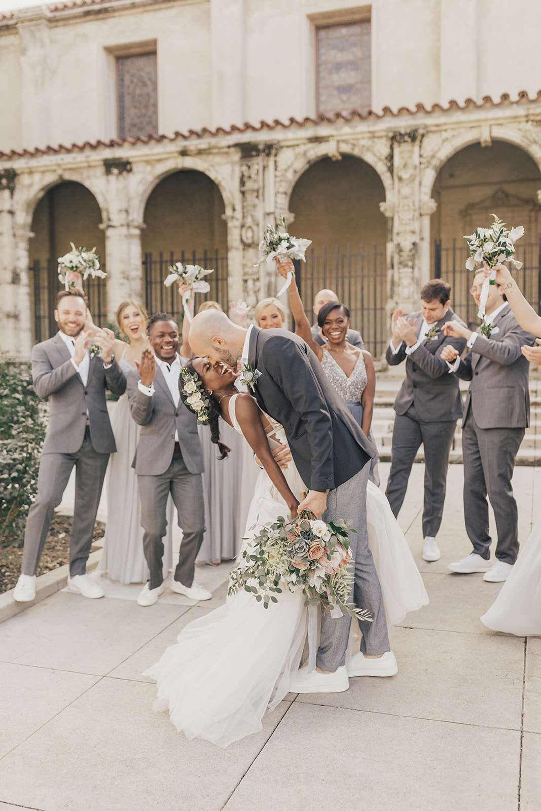 Bride and groom share a kiss surrounded by cheering wedding party